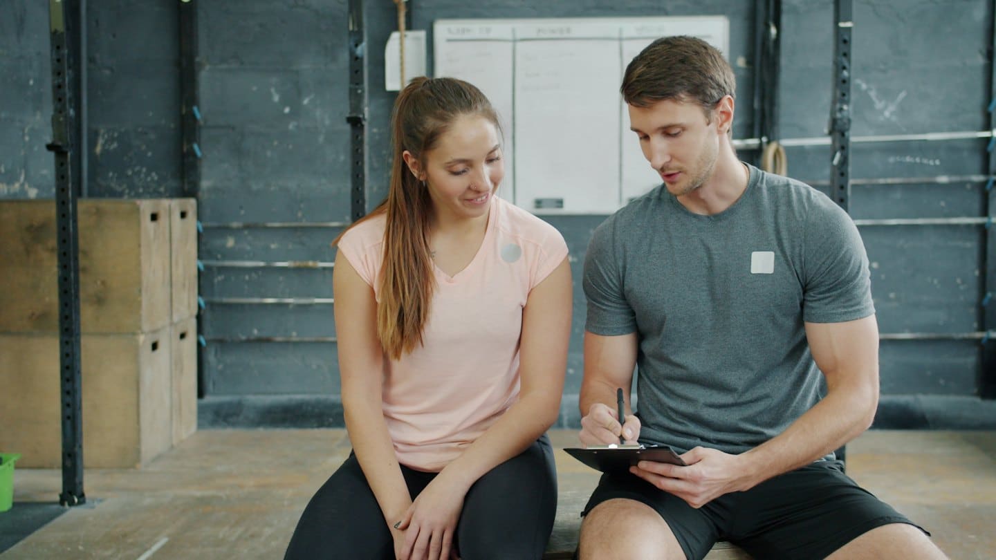 Un personal trainer scrive appunti su una lavagna per un cliente.
